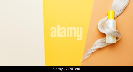 Fil de bouteille de shampooing sur boucle de verrou de cheveux blond sur fond orange coloré. Shampooing jaune pour bouteille. Bande de papier long plat de pose de l'espace de copie. Cheveux Banque D'Images