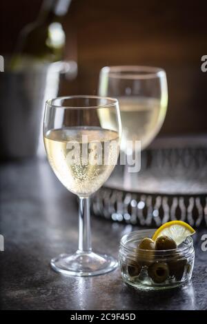 Vin blanc servi sur un plateau à boissons en métal bruni avec un plat d'olives. Arrière-plan sombre. Portrait Banque D'Images