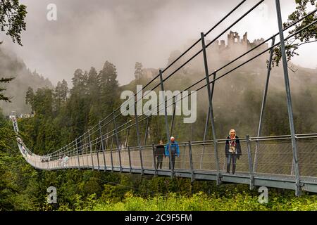 Angela Berg marche avec deux autres randonneurs sur le pont suspendu piéton Highline179 près de Reutte, dans le Tyrol, en Autriche ; les ruines du château d'Ehrenberg sont visibles dans la brume derrière eux. Le pont de 406 mètres enjambe la vallée à une hauteur allant jusqu'à 114 mètres et relie les ruines du château au Fort Claudia opposé ; depuis son ouverture en 2014 jusqu'en 2017, il détient le record du monde Guinness comme le plus long pont suspendu piéton du monde. Banque D'Images