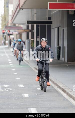 Un homme asiatique plus âgé et d'autres cyclistes à vélo dans une piste cyclable dédiée le week-end matin à Kent Street, Sydney, Australie Banque D'Images