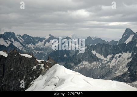 En regardant à travers les sommets d'une chaîne de montagnes déchiquetée, la neige couvre les zones de la roche avec des nuages gris clair dans le ciel. Banque D'Images