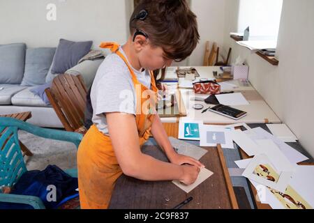 Un enfant mord une plaque de linocut sur une table d'artisanat tout en apprenant la gravure dans un atelier de classe d'art à Carmarthenshire Wales UK KATHY DEWITT Banque D'Images