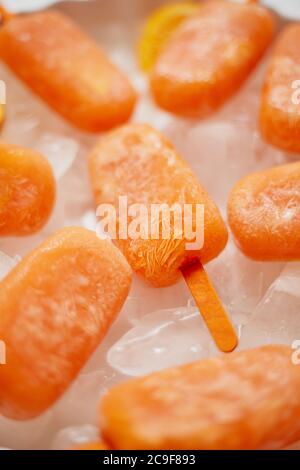 Popsicles congelés faits maison faits avec des oranges fraîches oragniques placées avec des glaçons sur une table en marbre Banque D'Images