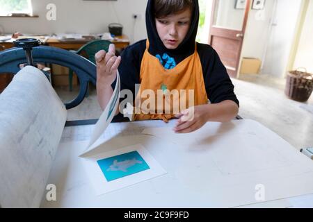 Garçon regardant des œuvres d'art en linocut sur une presse de gravure qu'il a fait dans un atelier d'art de gravure à Carmarthenshire pays de Galles Royaume-Uni KATHY DEWITT Banque D'Images