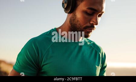 Gros plan d'un athlète debout à l'extérieur avec un casque. Homme de fitness écoutant de la musique pendant la course. Banque D'Images