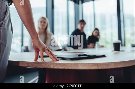 Femme directrice debout à table et s'adressant à son équipe assise dans la salle de réunion. Concentrez-vous sur la main d'une femme d'affaires à la table tout en discutant avec un collègue