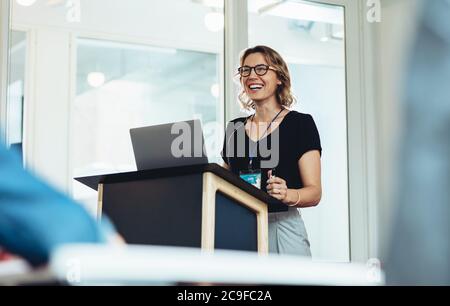 Femme d'affaires debout sur le podium avec un ordinateur portable pour prononcer un discours. Une femme professionnelle réussie s'adressant à un séminaire. Banque D'Images