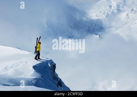Homme adulte se tient sur la falaise du sommet de la montagne avec sac à dos et ski observez le long panorama alpin pour le ski de fond Banque D'Images