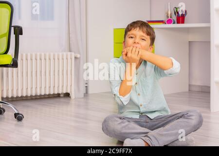 Petit garçon autiste mord les mains avec une forte expression négative du visage assis dans sa chambre, problème d'auto-blessure Banque D'Images