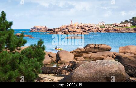 Des personnes faisant du kayak entre une formation rocheuse unique à la côte de granit rose près de Tregastel. Vieux phare en arrière-plan. Cotes-d'armure, Bretagne, France Banque D'Images