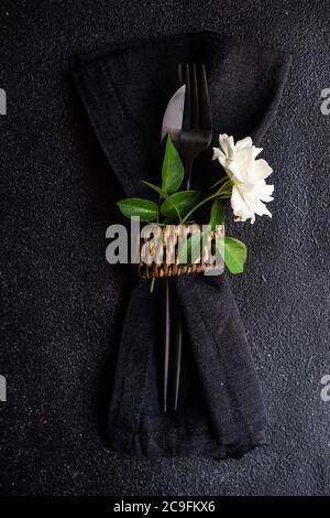 Table minimaliste en grès noir et couverts décorés de fleurs roses blanches sur une table en pierre noire avec espace de copie Banque D'Images