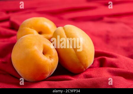 Trois abricots se trouvent sur une nappe rouge sur fond rouge Banque D'Images
