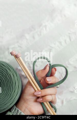 La main d'une femme tient un fil tricoté vert, le pliant en forme de coeur. Concept d'amour pour le tricot et l'artisanat. Banque D'Images