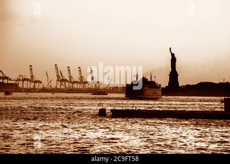 Le ferry de Staten Island navigue près de la Statue de la liberté au coucher du soleil. Banque D'Images