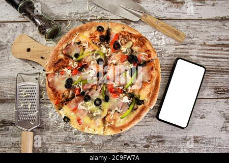 Vue de haut en bas sur les pizzas fraîches. Une délicieuse pizza à côté de l'écran vide du smartphone. Maquette de livraison de pizza. Banque D'Images