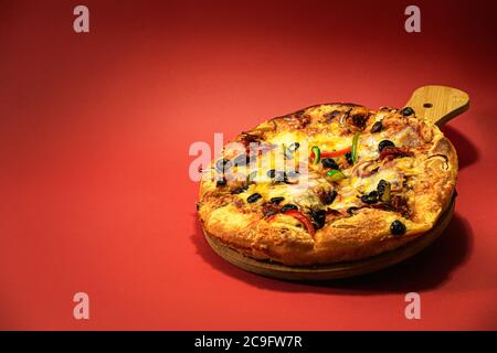 Pizza délicieuse avec fromage mozzarella, légumes, viande et tomates, isolée sur fond rouge, avec espace de copie disponible. Banque D'Images