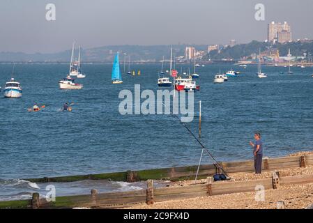 Pêche à la ligne sur la plage dans l'estuaire de la Tamise au large de Shoeburyness, Southend on Sea, Essex, Royaume-Uni. Bateaux au large de Thorpe Bay. Horizon de la ville de Southend. Des gens en canoës Banque D'Images