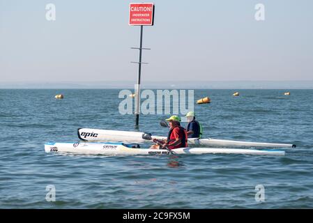 Deux mâles blancs de race blanche ravirant des canoës dans l'estuaire de la Tamise au large de Thorpe Bay, Southend on Sea, Essex, Royaume-Uni. Canoë-kayak dans la rivière. Obstructions sous l'eau Banque D'Images