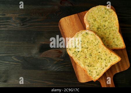 Vue de dessus de deux délicieux toasts faits maison au beurre d'ail sur un plateau de préparation servi sur une table brun foncé Banque D'Images