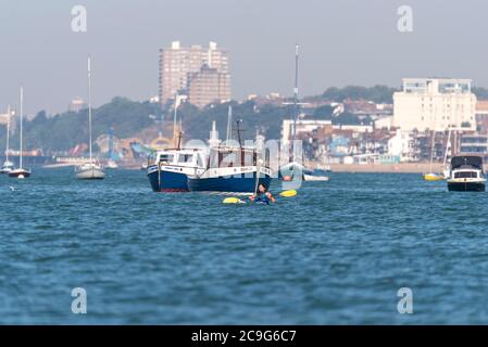 Une seule femme fait du kayak dans l'estuaire de la Tamise au large de Thorpe Bay, Southend on Sea, Essex, Royaume-Uni. Blanc caucasien femelle canoë avec des bateaux amarrés. Horizon de la ville Banque D'Images