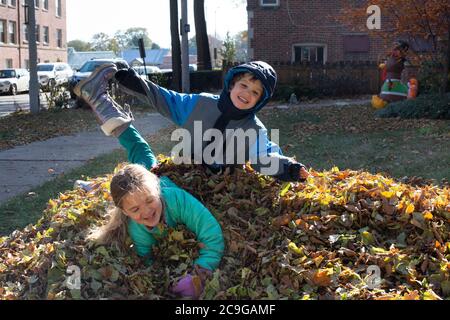 Heureux frères et sœurs sautant dans une pile de feuilles sur un journée d'automne froide Banque D'Images