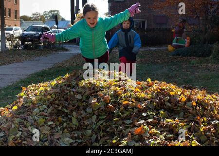 Des enfants heureux sautant dans une pile de feuilles sur un journée d'automne froide Banque D'Images