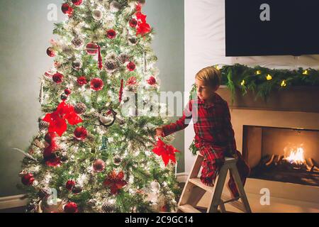 Garçon accrochant des ornements sur l'arbre de noël à la nuit Banque D'Images