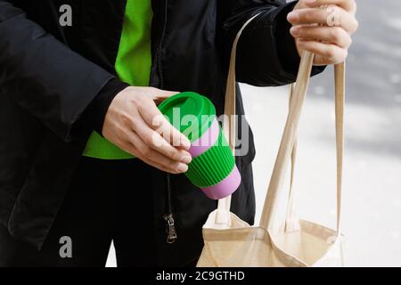 La main d'une femme tient une tasse de café écologique sur un fond de rue de ville, Banque D'Images