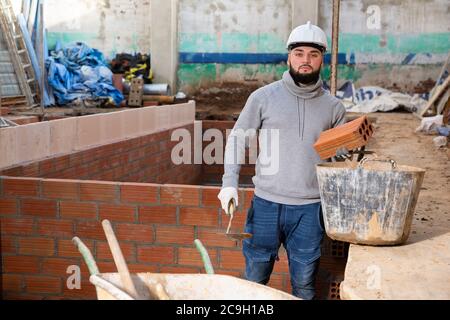 Jeune homme concentré travaillant sur ses rénovations de maison, l'installation de mur de brique à l'intérieur Banque D'Images