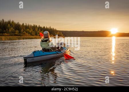 Kayakiste, fin des années quarante, blond, pagaies avec kayak gonflable au coucher du soleil sur un lac dans une ambiance de soirée, parc national de Muddus, Jokkmokk, Norrbotten laen Banque D'Images