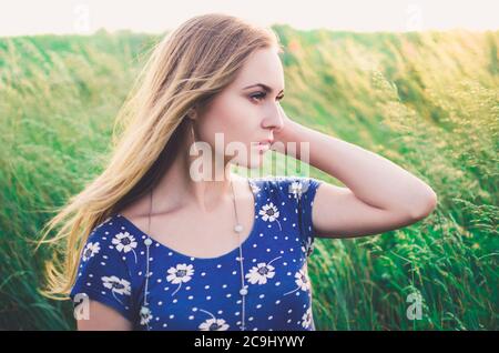 Blonde fille dans une robe bleue courte serrée s'asseoir dans l'herbe haute Banque D'Images