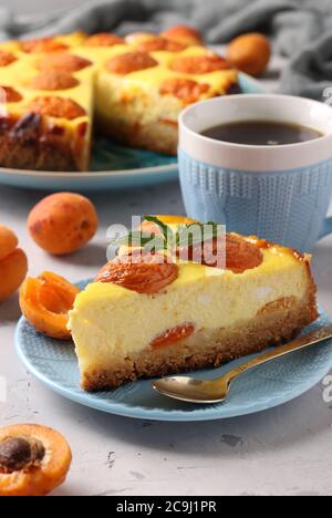 Cheesecake aux abricots avec un morceau découpé, situé sur une assiette bleue et une tasse de café, format vertical, gros plan Banque D'Images