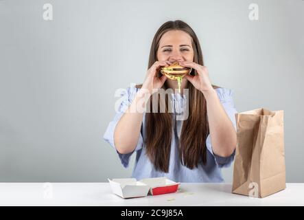 Portrait d'une belle jeune femme mangeant un hamburger, isolée sur fond blanc Banque D'Images