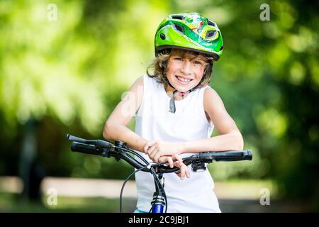 Garçon portant un casque de vélo et assis sur un vélo dans le parc, souriant, portrait. Banque D'Images