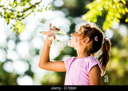 Fille de l'eau potable de bouteille en plastique dans le parc. Banque D'Images