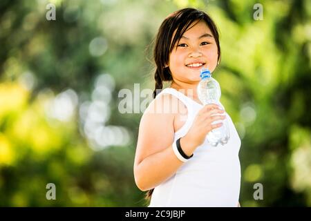 Fille debout avec une bouteille d'eau dans le parc, souriante, portrait. Banque D'Images