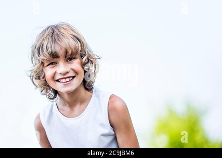 Garçon aux cheveux blonds souriant dans le parc, portrait. Banque D'Images