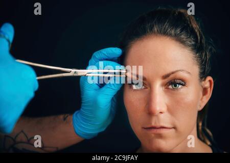 Portrait d'une belle jeune femme qui obtient son sourcil percé, corps piercer portant des gants bleus. Banque D'Images