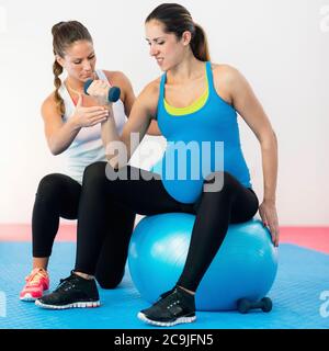 Exercice pendant la grossesse. Instructeur de fitness travaillant avec une femme enceinte. Entraînement simple avec haltères et ballon de fitness. Banque D'Images