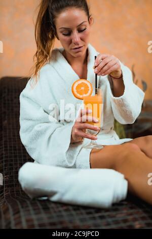 Femme en peignoir assise sur un lit de tepidarium et buvant de la limonade. Banque D'Images