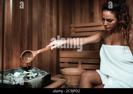 Femme avec une serviette assise sur un banc et se détendre dans un sauna chaud. Banque D'Images