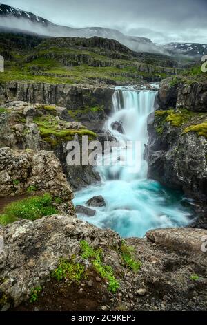 Une cascade mystérieuse se cachant dans une vallée en Islande. En été, il y a de petits arbres et de la mousse verte qui poussent le long des rochers. Spectaculaire et sombre t Banque D'Images