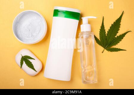 beauté, soins du corps cosmétiques avec extrait de marijuana sur fond jaune. bouteilles blanches avec cosmétiques et feuilles de cannabis. Banque D'Images