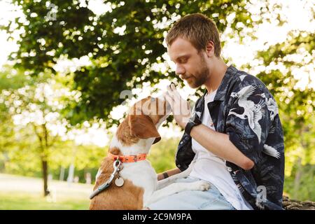 Image d'un jeune homme à barbe caucasien jouant avec son chien de beagle tout en marchant dans le parc d'été Banque D'Images