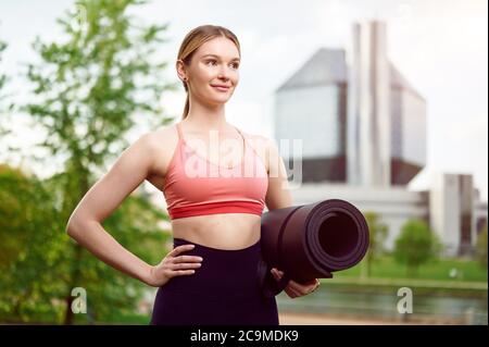 Femme de fitness portant des vêtements de sport tenant un tapis de yoga à l'extérieur dans le parc d'été Banque D'Images