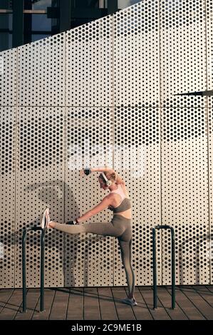 Musculeux mince de forme physique fille dans sportswear faisant l'exercice d'étirement devant le mur et l'écoute de la musique Banque D'Images