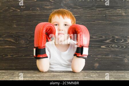 garçon aux cheveux rouges avec des gants de boxe rouges contre un mur en bois noir Banque D'Images