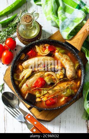 Ragoût de haricots, de légumes et de saucisses fumées avec sauce tomate dans la poêle sur une table en bois. Banque D'Images