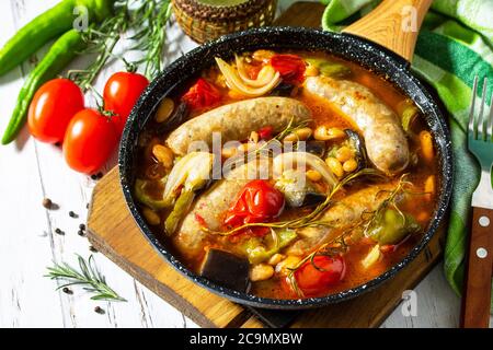 Ragoût de haricots, de légumes et de saucisses fumées avec sauce tomate dans la poêle sur une table en bois. Banque D'Images