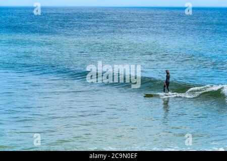 Surfeur surfant sur une petite vague sur une longue planche à voile en Floride, États-Unis Banque D'Images